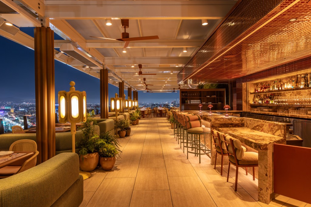Upscale rooftop bar and dining area at night with warm lighting, marble countertops, and city skyline views.